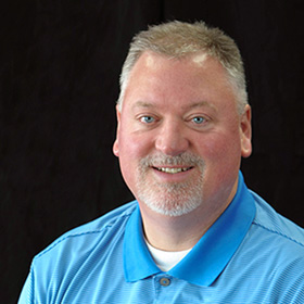 A man with grey hair and blue shirt smiling.